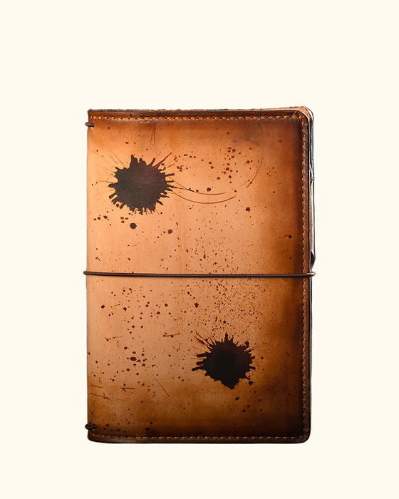 This is an example of what antiquing looks like on an Emma. Antiquing is when an artist applies dye to make markings like splatters and cup rings on a leather notebook to make it look older.
