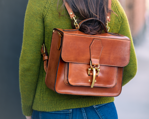 Woman whearing a boxy satchel with rounded corners and brass hardware,  green sweater and blue jeans