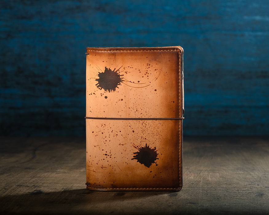 This is an example of what antiquing looks like on an Emma. Antiquing is when an artist applies dye to make markings like splatters and cup rings on a leather notebook to make it look older.